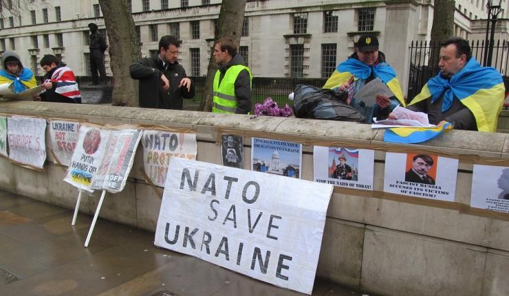 People behind a wall posted with signs, with one sign prominently stating "NATO save Ukraine"